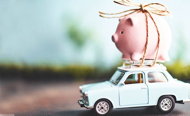 Piggy bank strapped to the top of a toy car.